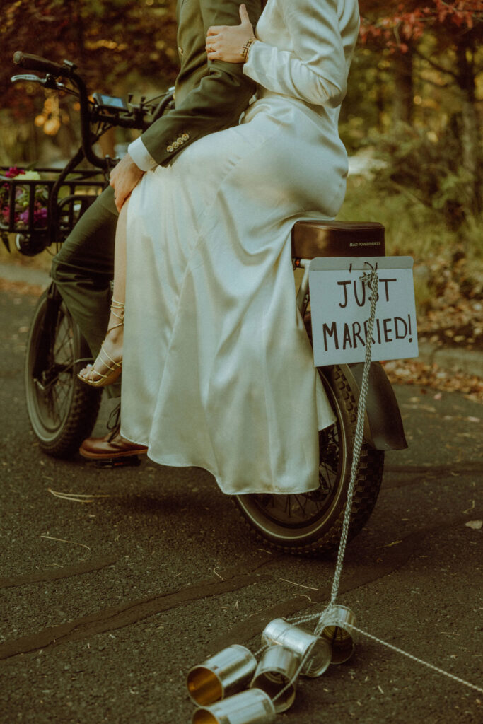bride and groom destination wedding portrait on bike with sign that says "just married" 