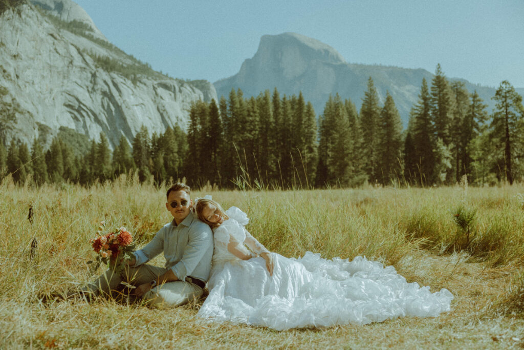 bride and groom sitting down in field in yosemite national park for their elopement photos