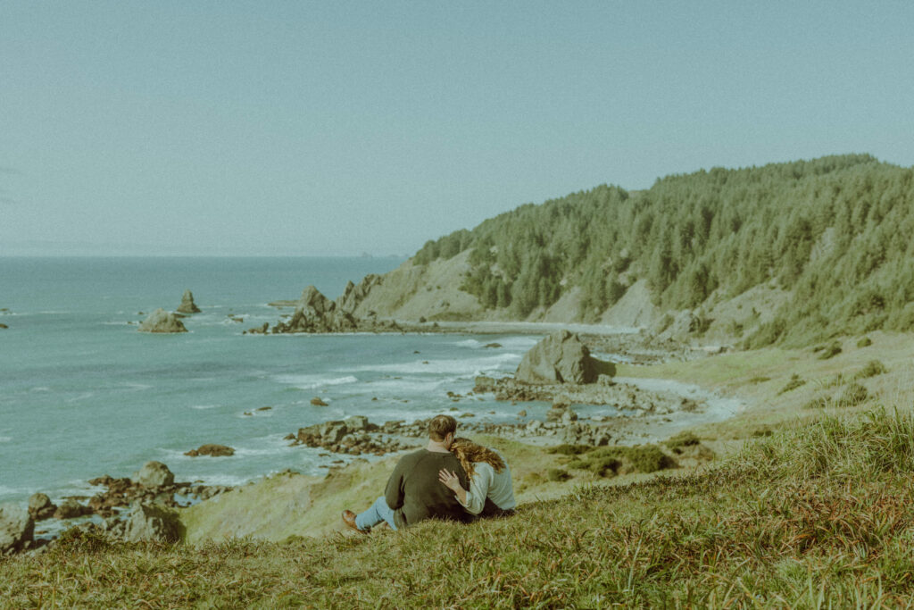 couple sitting on a grassy hill for their destination engagement photos at Samuel H Boardman state park on the oregon coast
