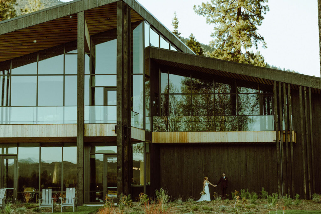 exterior photo of black butte ranch wedding venue with bride and groom holding hands