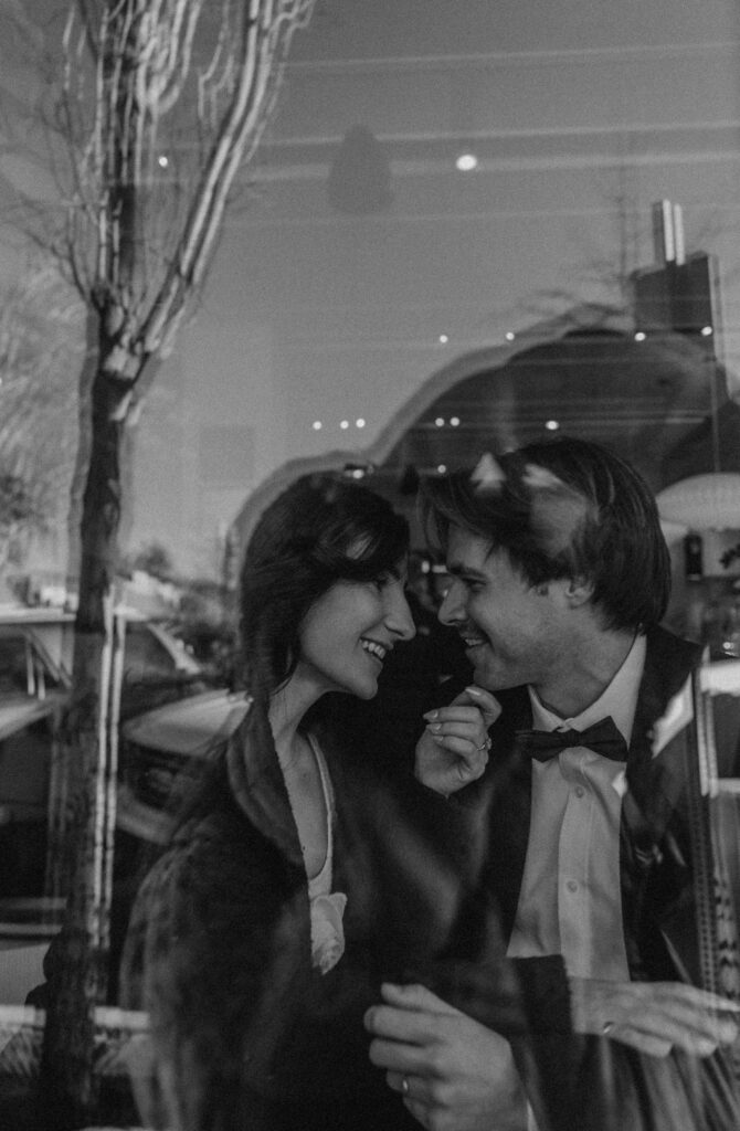 bride and groom facing eachother in a cafe looking through a window