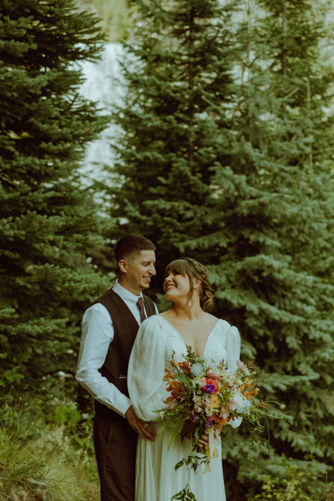 bride and groom pose with tumalo falls in the background on their wedding day in the forest of bend oregon