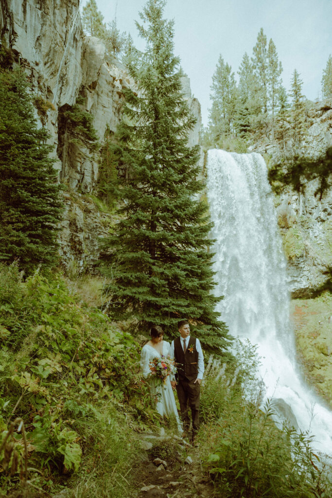 bride and groom pose with tumalo falls in the background on their wedding day 