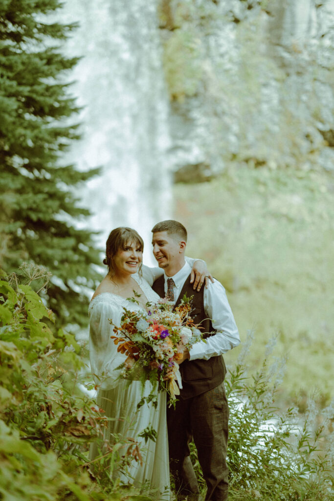 bride and groom pose with tumalo falls in the background on their wedding day 