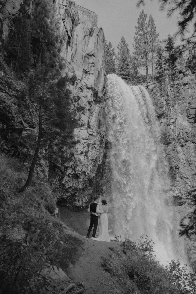 bride and groom pose with tumalo falls in the background on their wedding day 