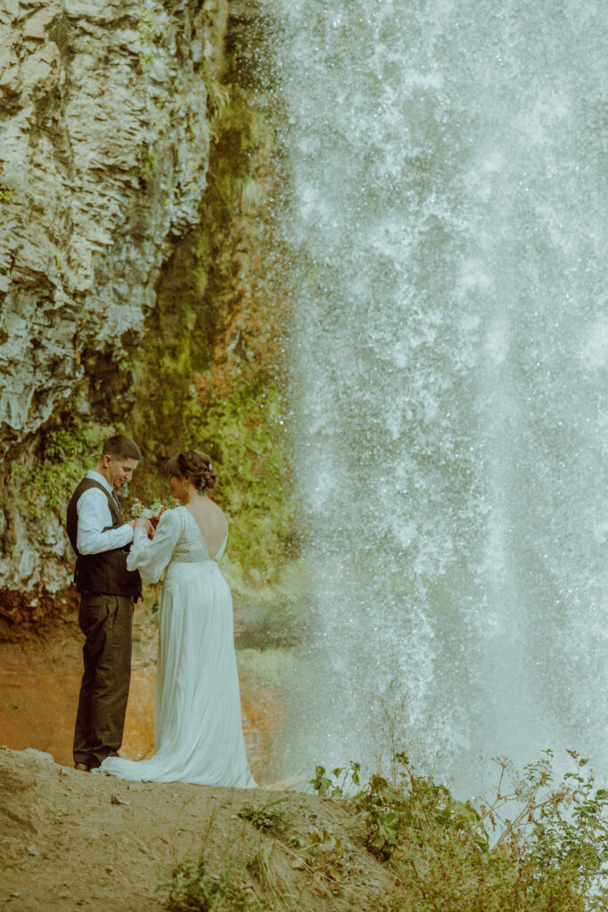 bride and groom pose with tumalo falls in the background on their wedding day 