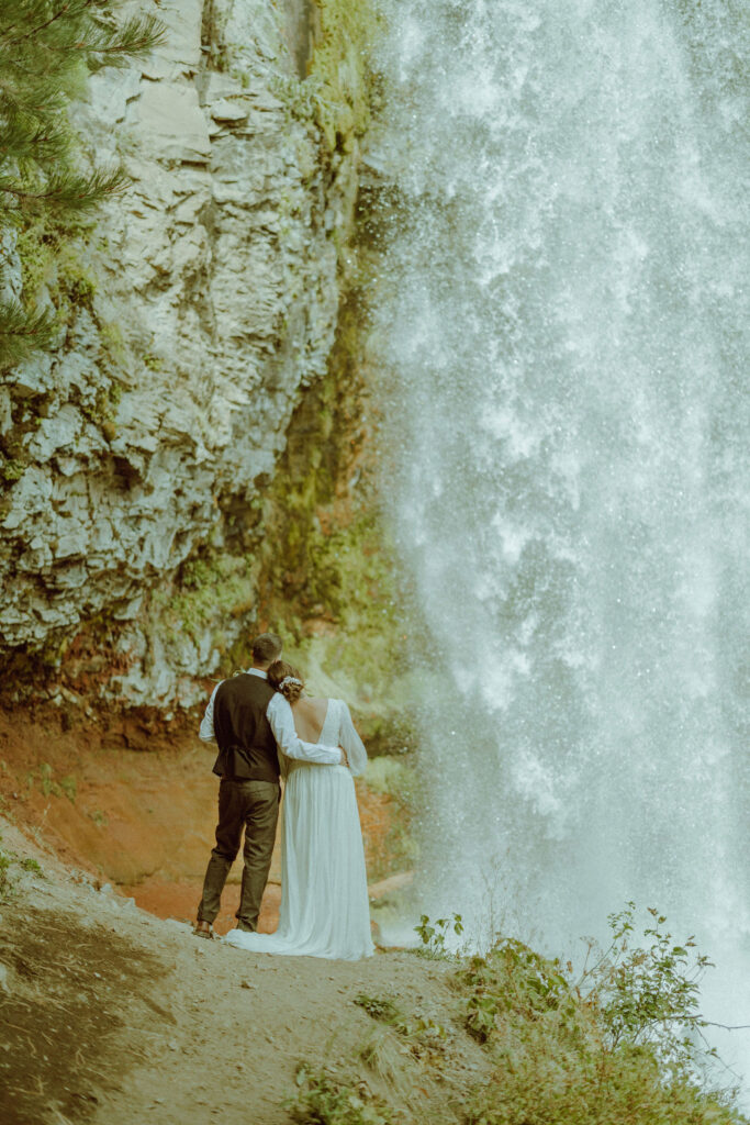 bride and groom pose with tumalo falls in the background on their wedding day 