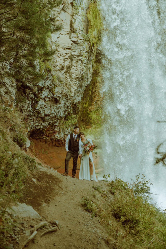 bride and groom pose with tumalo falls in the background on their wedding day 