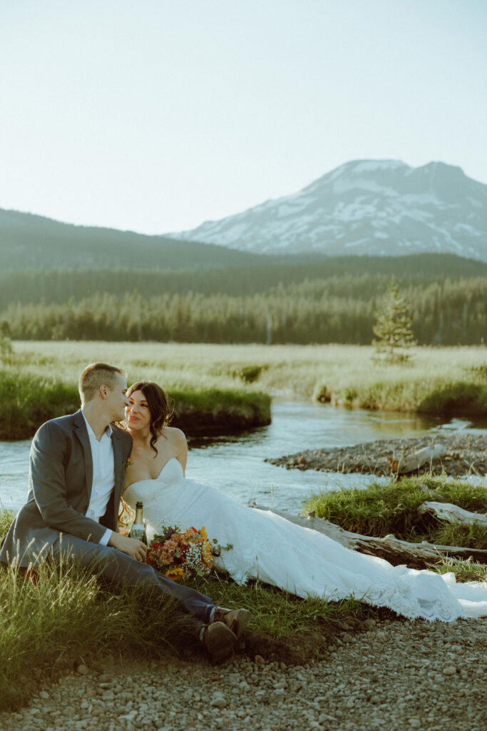  bride and groom sitting on creek bank at sparks lake oregon elopement