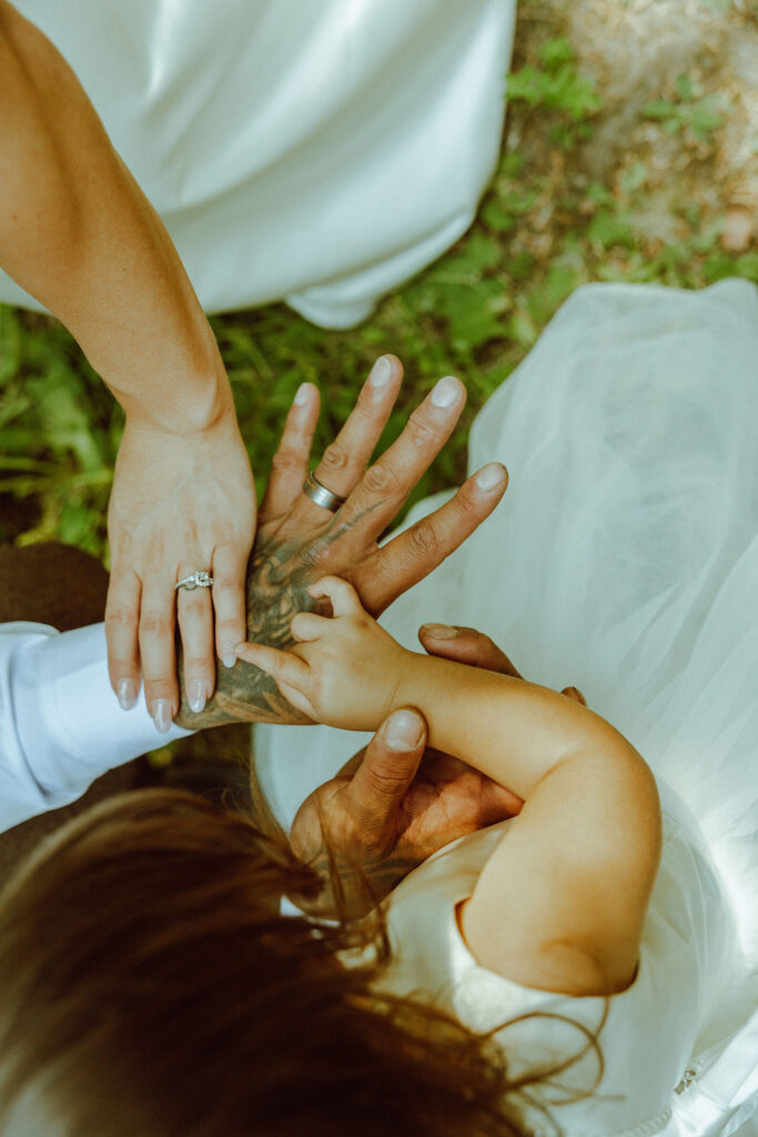 bride and groom in forest showing wedding rings to their daughter