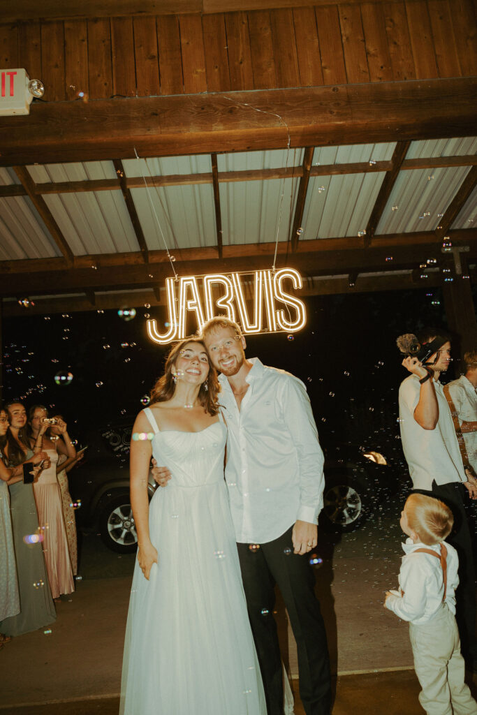 bride and groom posing for photo in front of neon sign at wedding in oregon