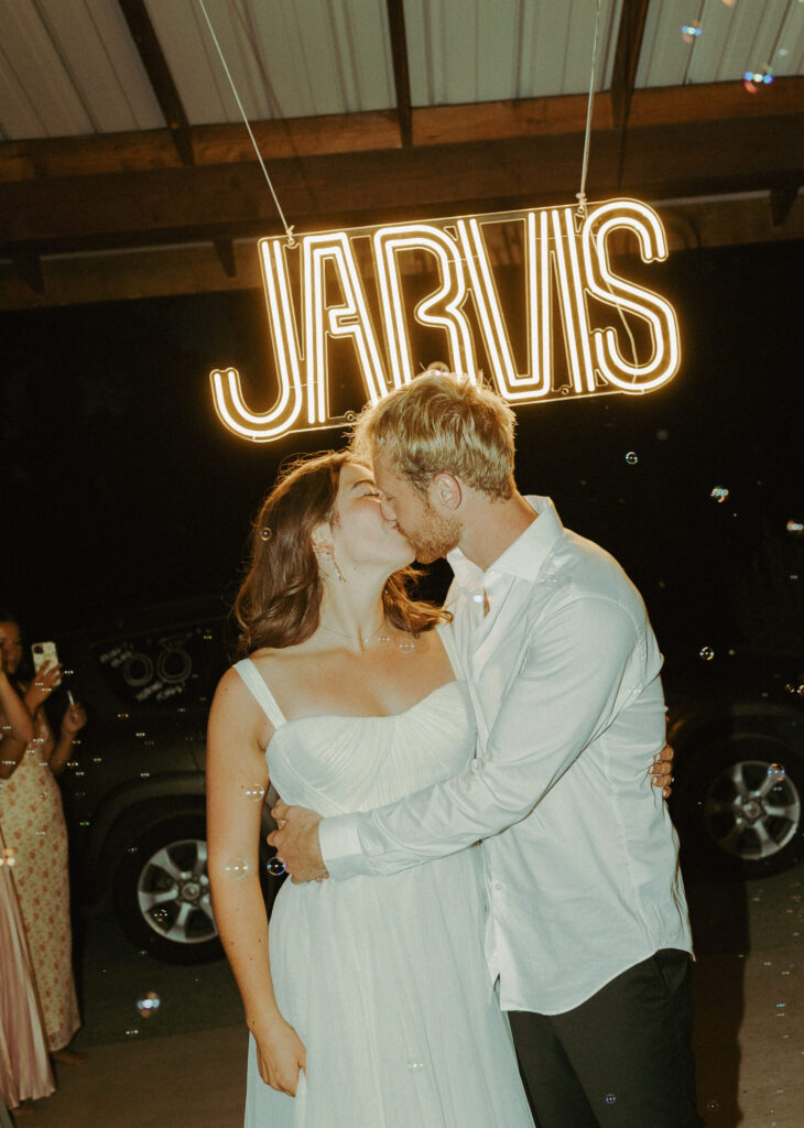 bride and groom kissing for photo in front of neon sign at wedding in oregon