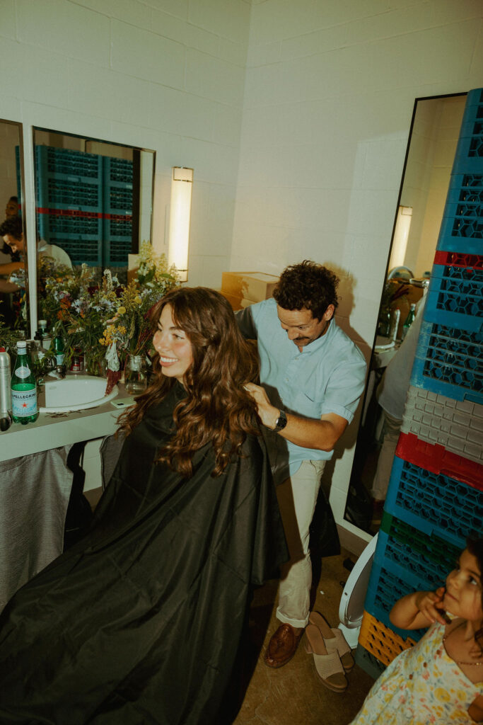 bride getting her hair chopped by hair stylist at wedding reception