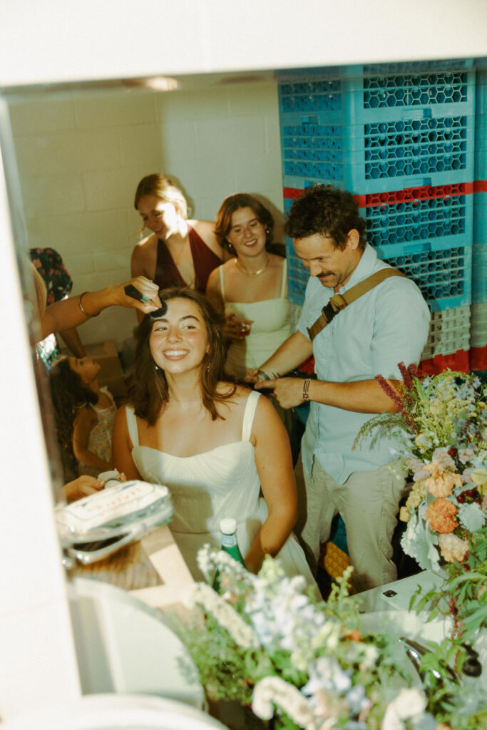 bride getting her hair chopped by hair stylist at wedding reception